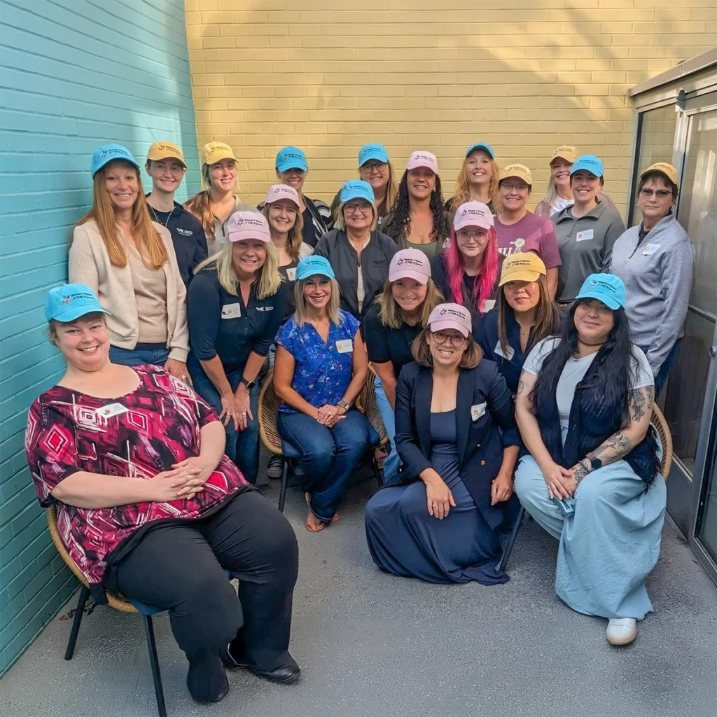 Group of people in baseball caps pose for photo against brick walls